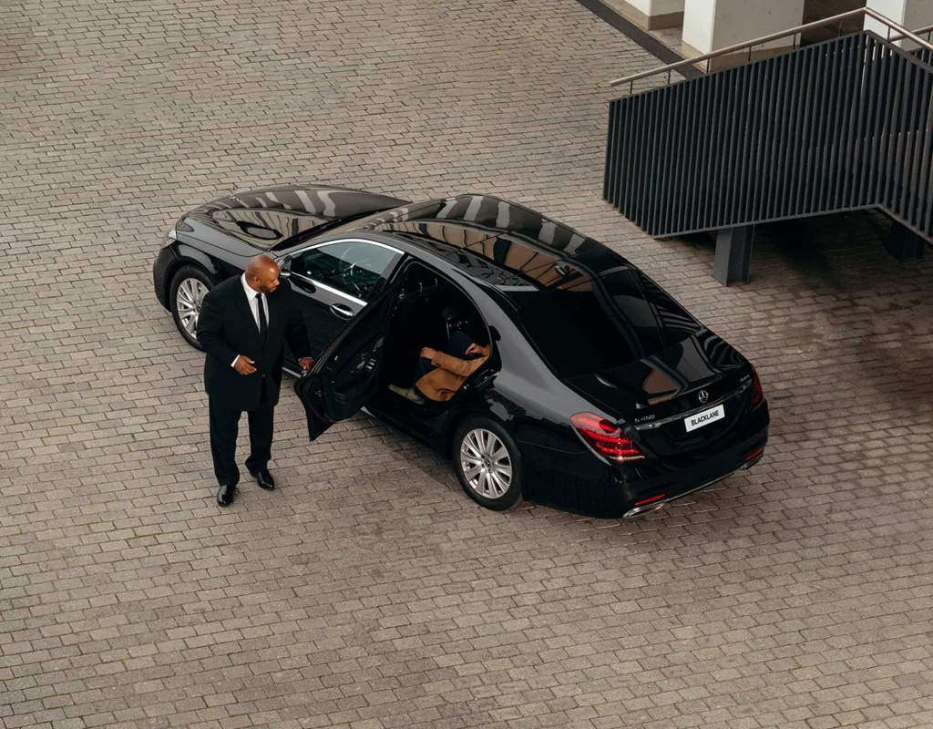 Man standing beside an open door of a black luxury limousine, captured from above, representing Limo Cost Per Hour in Canada